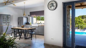 Een moderne keuken met een eethoek, een klok aan de muur en uitzicht op een zwembad.