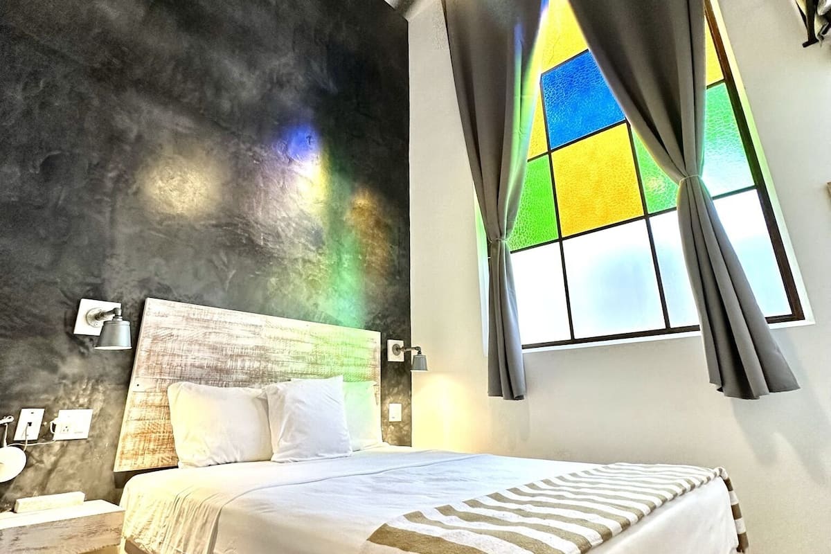 Ein modernes Schlafzimmer mit einem großen Bett, einem Deckenventilator, einem Buntglasfenster und Holzboden.