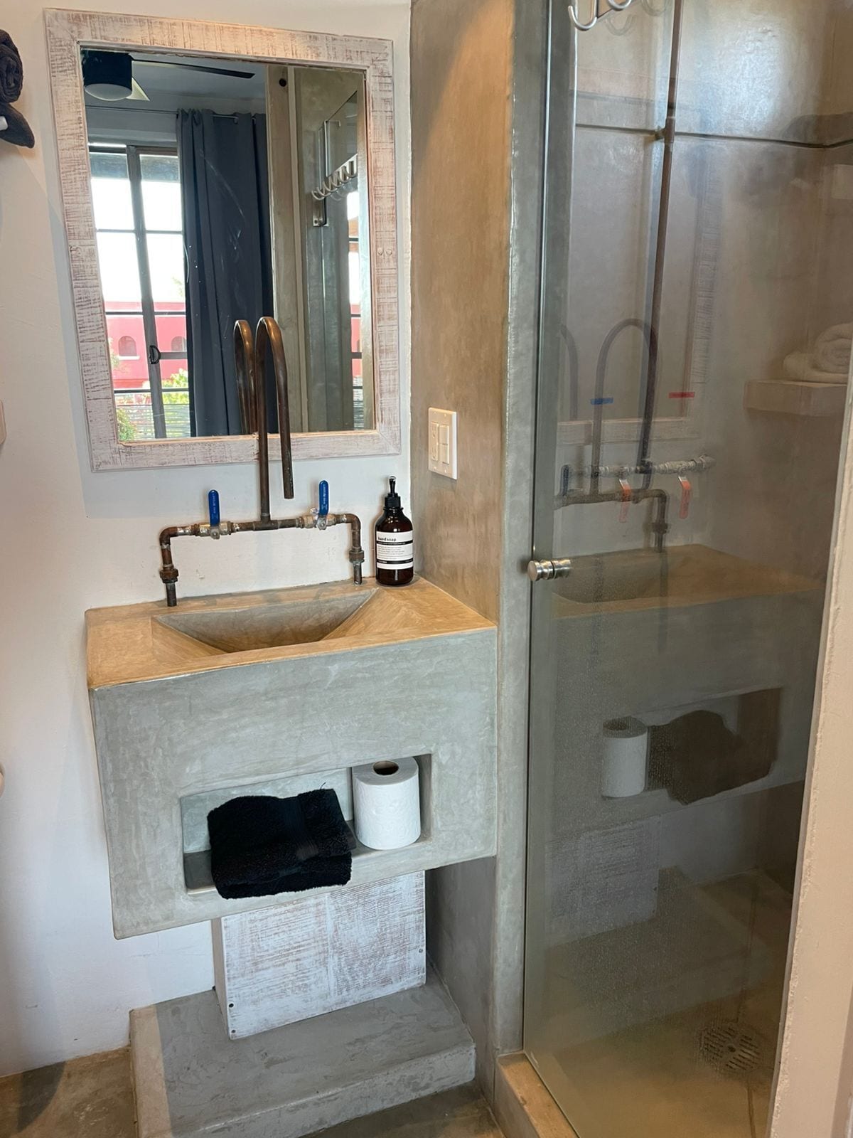 Un baño con un espejo grande, un lavabo con una toalla y una zona de ducha con paredes de vidrio.