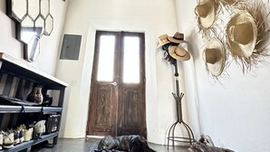 A room with a wooden door, a black dog lying on the floor, a shelf with shoes, and a wall with hats. - Baja House (Todos Santos)