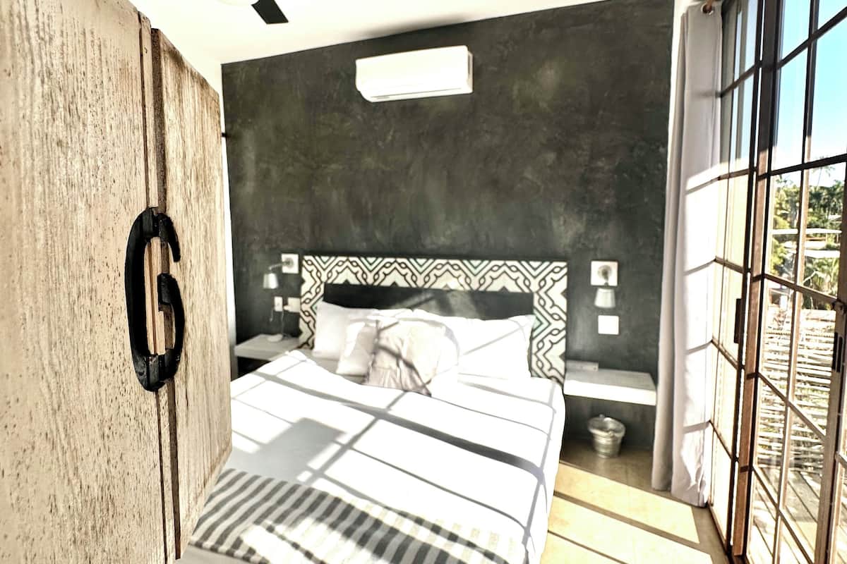 Ein modernes Schlafzimmer mit einem Bett, einem Deckenventilator, einem großen Fenster und einem Holzschrank.