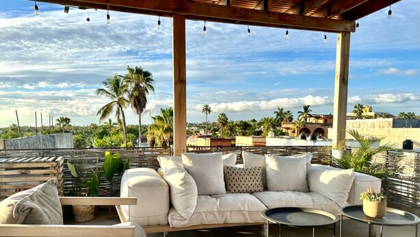 A covered outdoor seating area with a white sofa, a small round table, and potted plants. - Baja House (Todos Santos)