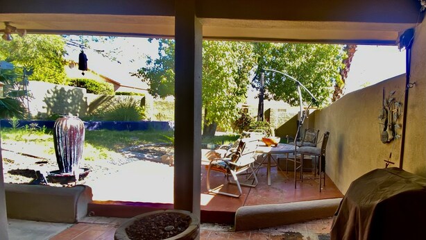 A patio area with a stone planter, a table with chairs, and a view of a garden and trees.