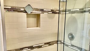 A glass-enclosed shower with beige tiles and a small shelf.