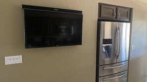 A kitchen with a built-in stainless steel refrigerator and a wall-mounted flat-screen TV.