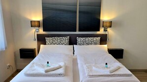 A double bed with white linens, two bedside tables with lamps, and a large abstract painting above the bed.