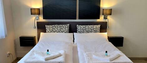 Una cama doble con ropa blanca, dos mesitas de noche con lámparas y un cuadro abstracto grande sobre la cama.