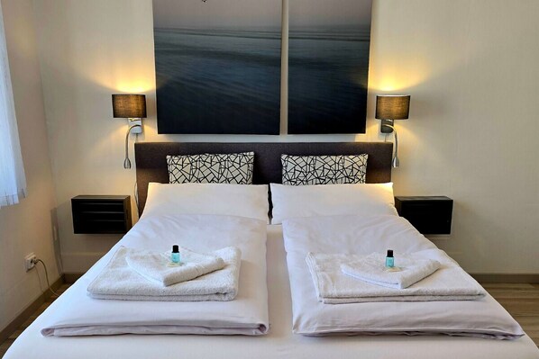 A double bed with white linens, two bedside tables with lamps, and a large abstract painting above the bed. - STAYaWHILE apartment comfort | 5 min to Bali Therme + GOP, NETFLIX (Bad Oeynhausen)