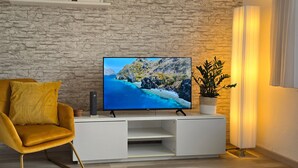 A modern living room with a stone wall, a flat-screen TV, a yellow armchair, a white entertainment unit, and a potted plant.