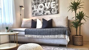 A living room with a sofa, pillows, a round coffee table, a floor lamp, a wall art piece with the word "LOVE", and a potted plant.