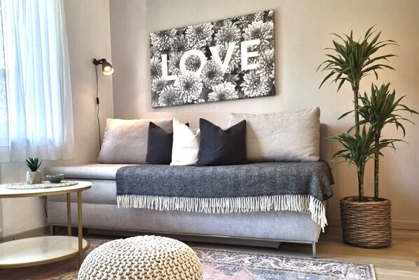 A living room with a sofa, pillows, a round coffee table, a floor lamp, a wall art piece with the word "LOVE", and a potted plant.
