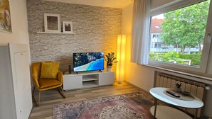 A modern living room with a stone wall, a sofa, a TV, a small table, and a view of a residential area.