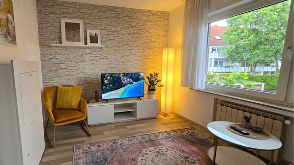 Una sala de estar moderna con una pared de piedra, un sofá, un televisor, una mesita y vistas a una zona residencial.