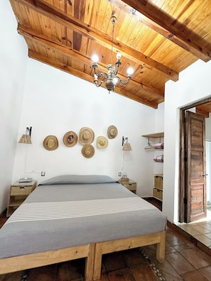 Un dormitorio con techo de madera, una cama con colcha a rayas y varios sombreros colgados en la pared.