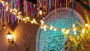 Un mur décoratif orné d’une mosaïque de galets et d’une statue de Bouddha, le tout entouré de plantes en pot et illuminé de guirlandes lumineuses.