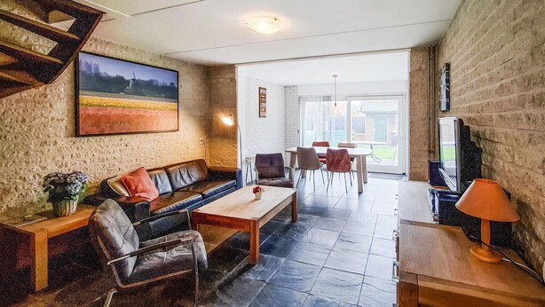 Un salon avec un canapé, des fauteuils, une table basse, un téléviseur et un tableau accroché au mur.