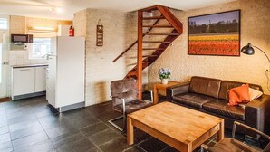 Un salon avec une table en bois, un canapé, un fauteuil, un escalier, un coin cuisine et un tableau au mur.