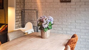 Un coin repas avec une table en bois, un panier en osier rempli de fleurs et un mur de briques orné d’une pancarte sur laquelle on peut lire « PLEIN D’HUMOUR ».