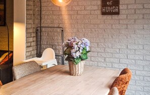 A dining area with a wooden table, wicker basket with flowers, and a brick wall with a 'of HUMOR' sign. - Amazing home in Callantsoog with WiFi (Callantsoog)
