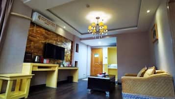 A living room with a sofa, a coffee table, a TV, and a small kitchen area with a microwave and a toaster.