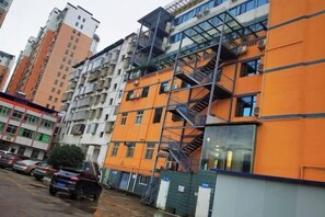 Un immeuble à plusieurs étages aux façades orange et blanches, avec un escalier apparent et des voitures garées devant.