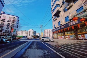 Una calle con edificios, un restaurante con faroles rojos y un coche blanco estacionado al lado.