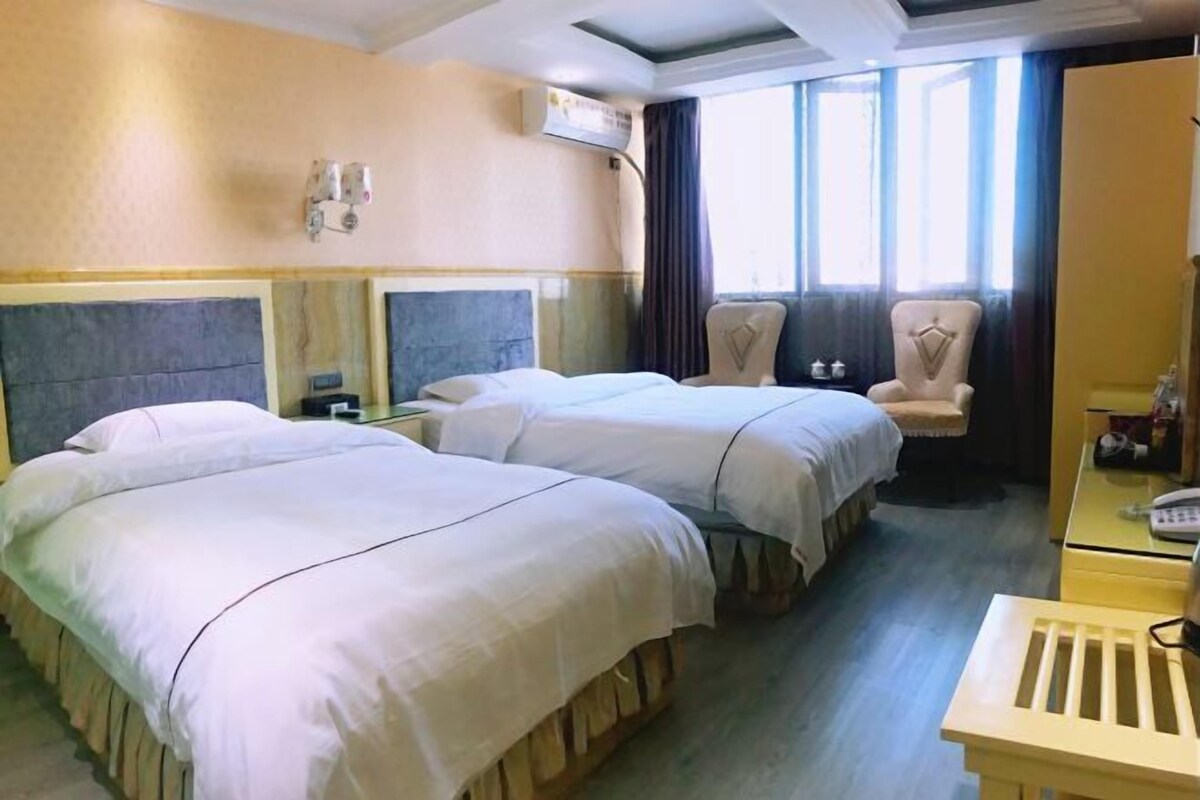 Une chambre d’hôtel avec deux lits, un bureau, une chaise et une fenêtre avec des rideaux.