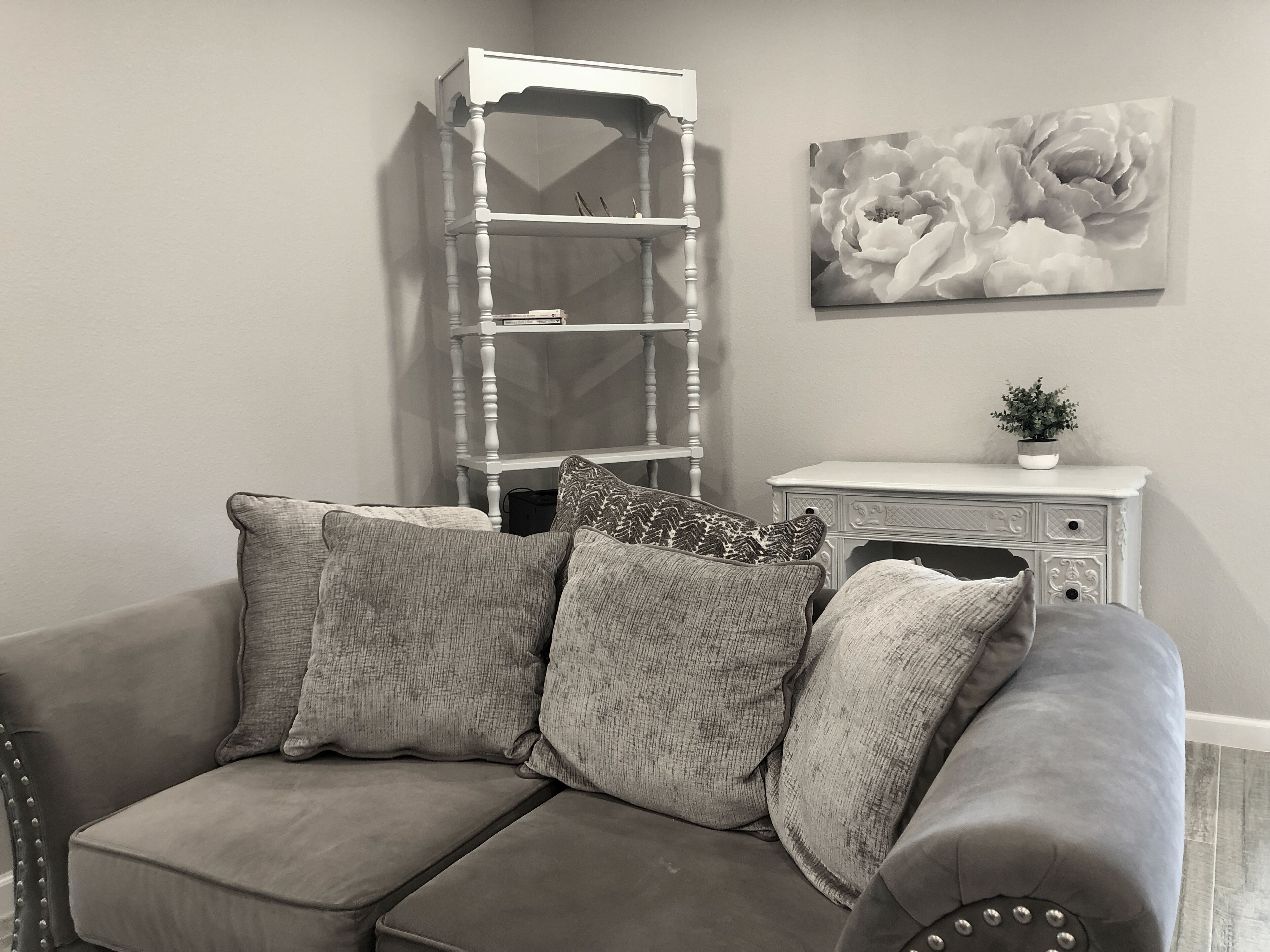 Un divano modulare grigio con cuscini decorati, un mobile contenitore bianco con una pianta e un quadro floreale appeso al muro.