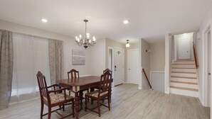 Une salle à manger avec une table et des chaises en bois, un lustre et un escalier menant à une autre pièce.