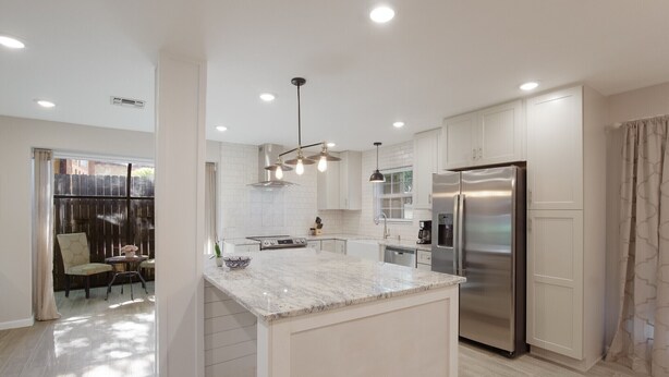 Une cuisine moderne avec des meubles blancs, un îlot central, des appareils en acier inoxydable et des luminaires suspendus.