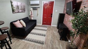 A living room with a black sofa, a dining table with four chairs, a red door, and a fireplace. - Cozy & Convenient Bungalow - Downtown & HPU (Brownwood)