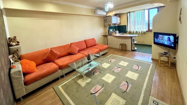 Uma sala de estar com sofá, mesa de centro, televisão e cozinha.