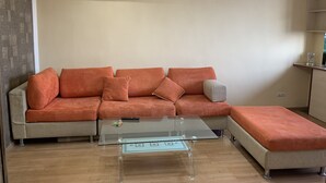 Uma sala de estar com sofá seccional, mesa de centro de vidro e pequena mesa lateral.