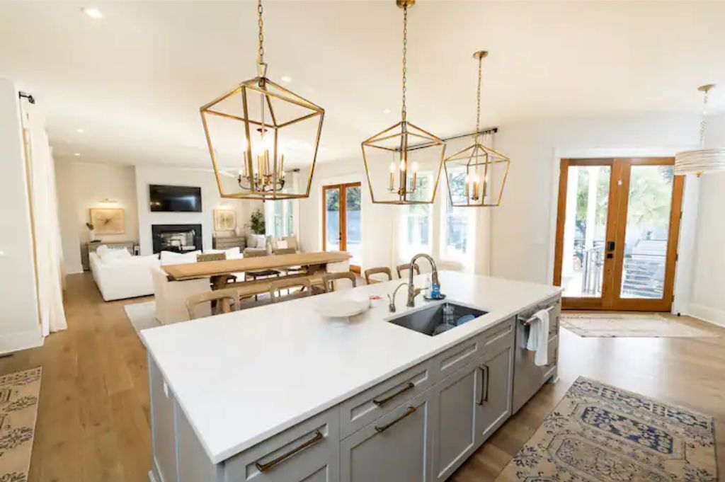 A modern kitchen with a central island, pendant lights, and a view to the dining area.