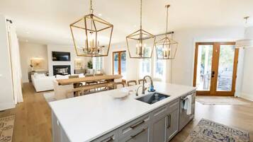 A modern kitchen with a central island, pendant lights, and a view to the dining area.