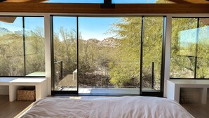 Un dormitorio con una cama grande, vigas de madera en el techo y vistas a un paisaje montañoso a través de ventanales.