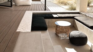 Un espacio al aire libre moderno con una terraza de madera, asientos acolchados e iluminación colgante de fibras.