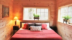A cozy wooden cabin bedroom with a large bed, a window with a view, and a nightstand with a lamp. - Romantic Retreat • Hottub, Gazebo, Firepit, ~Game,Kayak, Lake access & Fishing (Sevierville)