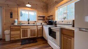 A wooden cabin kitchen with a large window, wooden cabinets, a stove, and a refrigerator. - Romantic Retreat • Hottub, Gazebo, Firepit, ~Game,Kayak, Lake access & Fishing (Sevierville)
