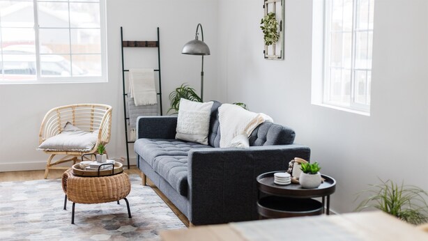 Una sala moderna con un sofá gris, una silla de mimbre, una mesita y una lámpara de pie.