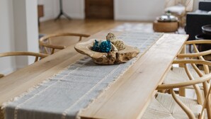 Una mesa de comedor de madera con un camino tejido, rodeada de sillas de mimbre.