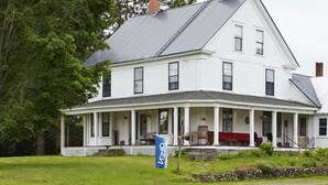 A two-story white house with a covered porch, a chimney, and a flag.