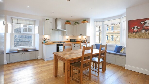 A modern kitchen with white cabinets, a wooden dining table, and built-in seating.