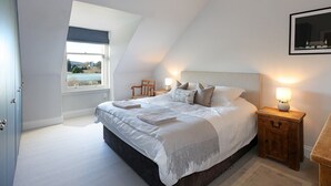 A bedroom with a large bed, a nightstand with a lamp, a window with a view, and a door.