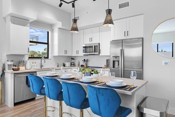 A modern kitchen with white cabinets, stainless steel appliances, and blue bar stools.