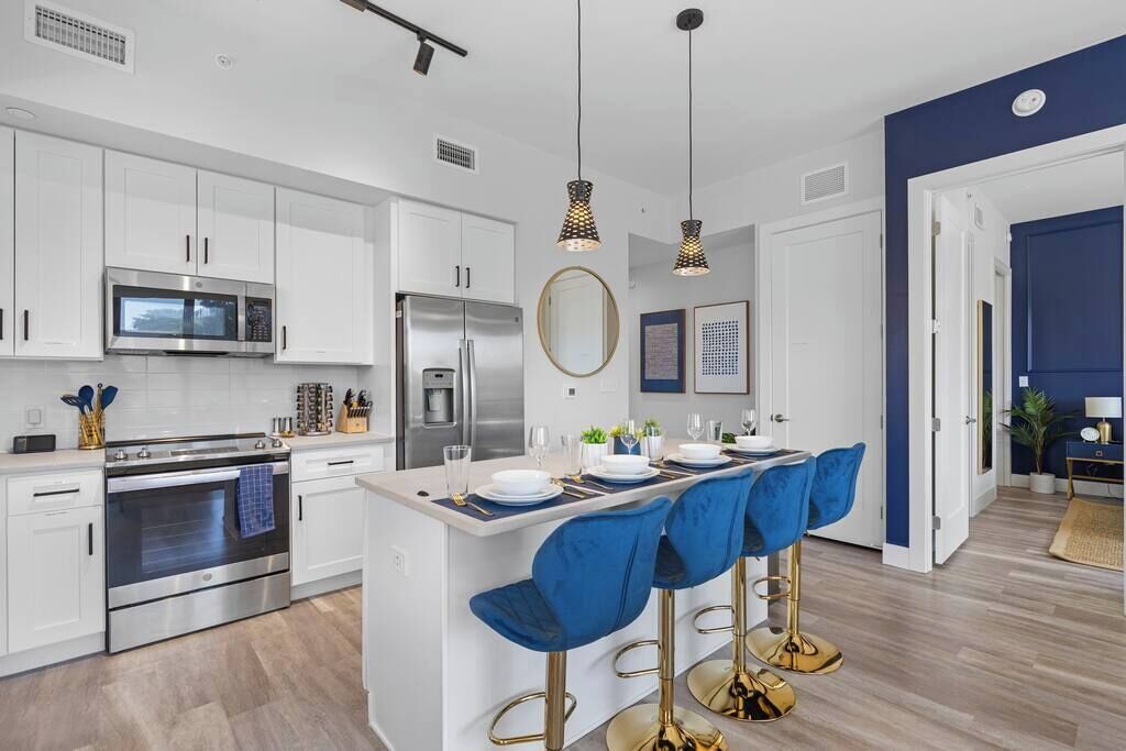 Una cocina moderna con armarios blancos, electrodomésticos de acero inoxidable y una isla central con taburetes azules.