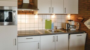 Una cocina con armarios blancos, un microondas de acero inoxidable, un hervidor y una cafetera.