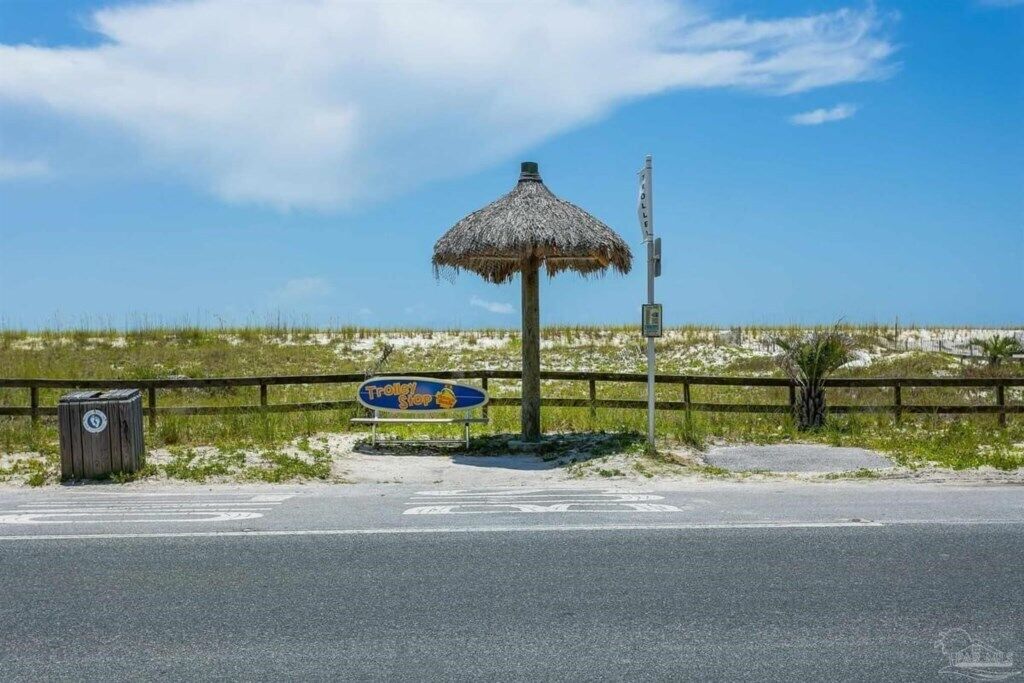 Un endroit situé au bord de la plage, avec un parasol en chaume, un panneau indiquant un arrêt de tramway et une clôture en bois.