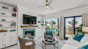 Ein modernes Wohnzimmer mit Kamin, bequemen Sitzgelegenheiten, einem Flachbildfernseher und Blick ins Freie.