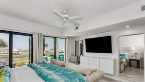 Ein modernes Hotelzimmer mit einem großen Bett, einer Couch, einem an der Wand befestigten Fernseher und einem Balkon mit Blick auf den Strand.